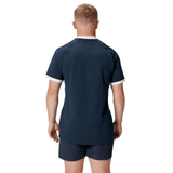 A person with short blond hair is wearing the British & Irish Lions 2025 Training Jersey by Canterbury, featuring ergonomically placed panels for comfort, paired with navy blue shorts, and is standing with their back to the camera.