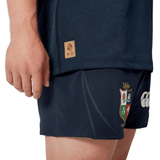 A person in a dark sports outfit is wearing the British & Irish Lions 2025 Training Jersey by Canterbury, which features ergonomically placed panels, along with shorts embellished with the colorful crest and logo of the British & Irish Lions.