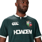 A man wearing the British & Irish Lions 2025 Training Jersey by Canterbury, featuring logos and "Howden" text. This stylish, dark green piece is crafted from recycled polyester for an eco-friendly touch.