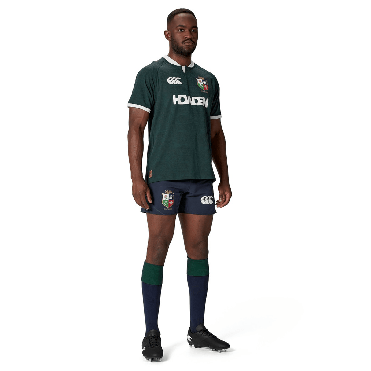 A man is standing in the British & Irish Lions 2025 Training Jersey by Canterbury, paired with navy shorts and knee-high socks.