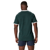 A person wearing the British & Irish Lions 2025 Training Jersey by Canterbury, made of recycled polyester in dark green, matched with dark shorts, stands facing away from the camera against a white background.