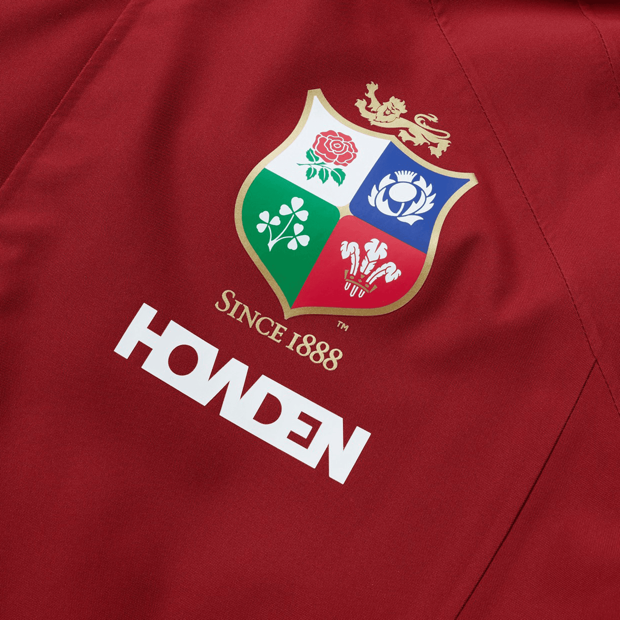 Close-up of a red polyester jacket featuring a rugby emblem with four national symbols and "Since 1888" above the Canterbury brand name. This waterproof jacket captures the essence of the British & Irish Lions and is part of their 2025 collection by Canterbury.