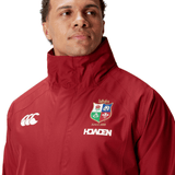 A person wearing the British & Irish Lions 2025 Waterproof Jacket by Canterbury, crafted from polyester in a red hue, showcasing the lion and crest logo of the British & Irish Lions with "SINCE 1888" text.