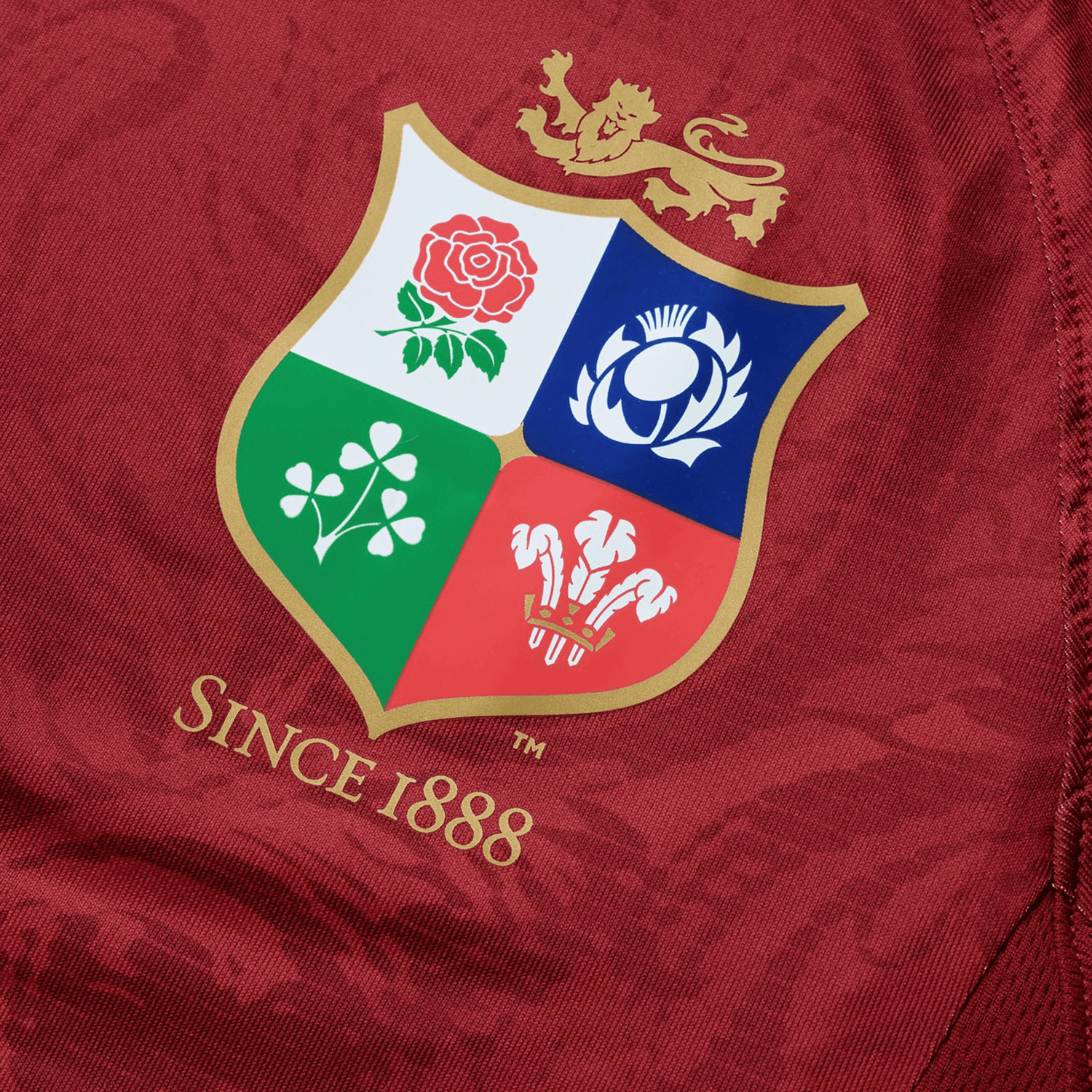 The British & Irish Lions 25 Superlight Training Tee by Canterbury, crafted by Canterbury, features a red fabric with a gold-trimmed crest that displays symbols of a rose, thistle, shamrock, and three feathers beneath a lion. The text reads "Since 1888.