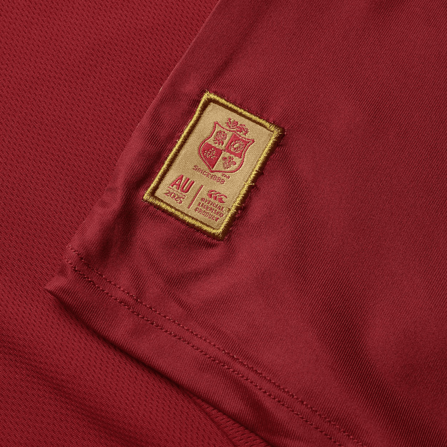 The British & Irish Lions 25 Superlight Training Tee by Canterbury is a maroon sports jersey featuring a gold embroidered patch with a shield, "AU 2023" text, and brand logos. This tee is ideal for intense sessions and embodies Canterbury's renowned quality.