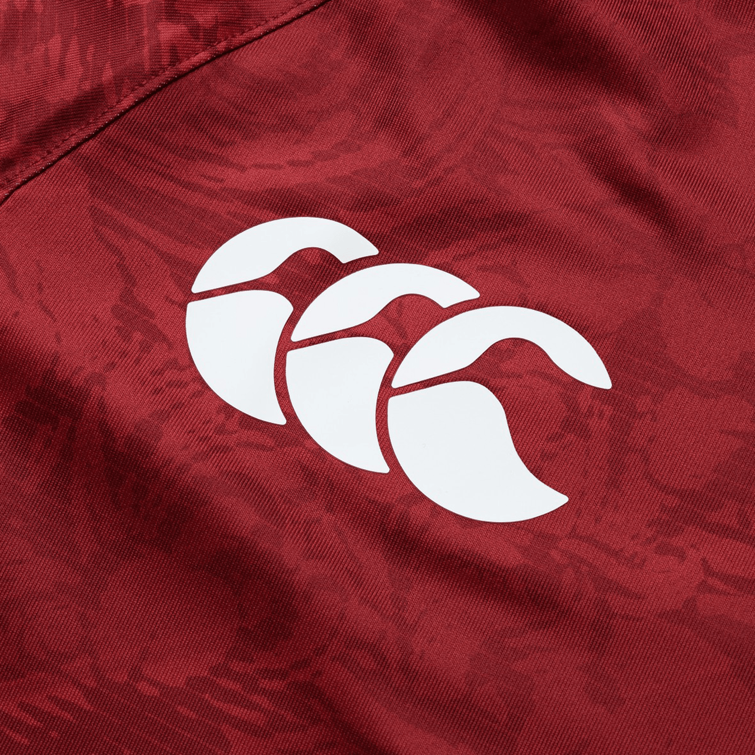 Close-up of a red fabric from the British & Irish Lions 25 Superlight Training Tee by Canterbury, showcasing a white, three-leaf logo reminiscent of the iconic British & Irish Lions design.