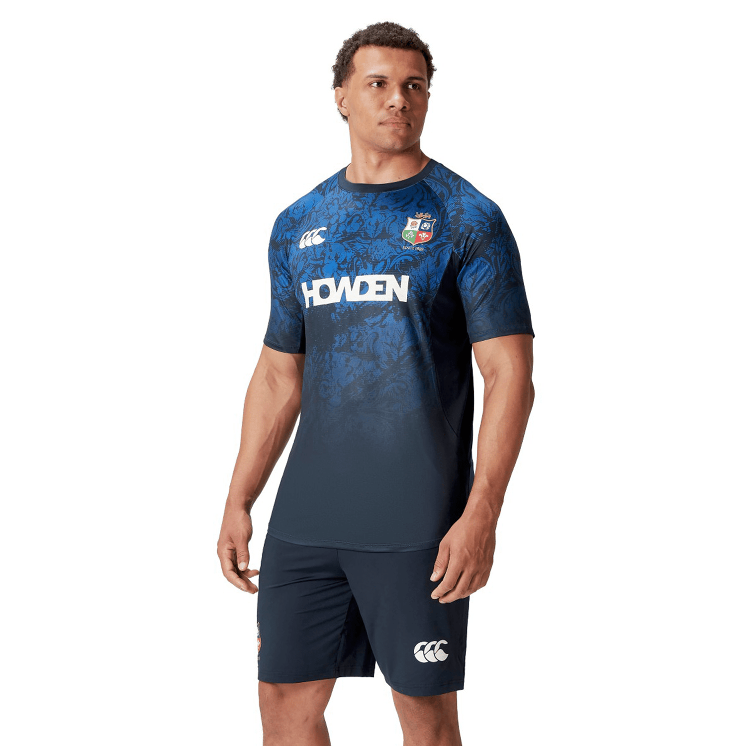 A man dons a British & Irish Lions 25 Superlight Training Tee by Canterbury, featuring "Howden" and Canterbury logos, while he gazes thoughtfully to the side.