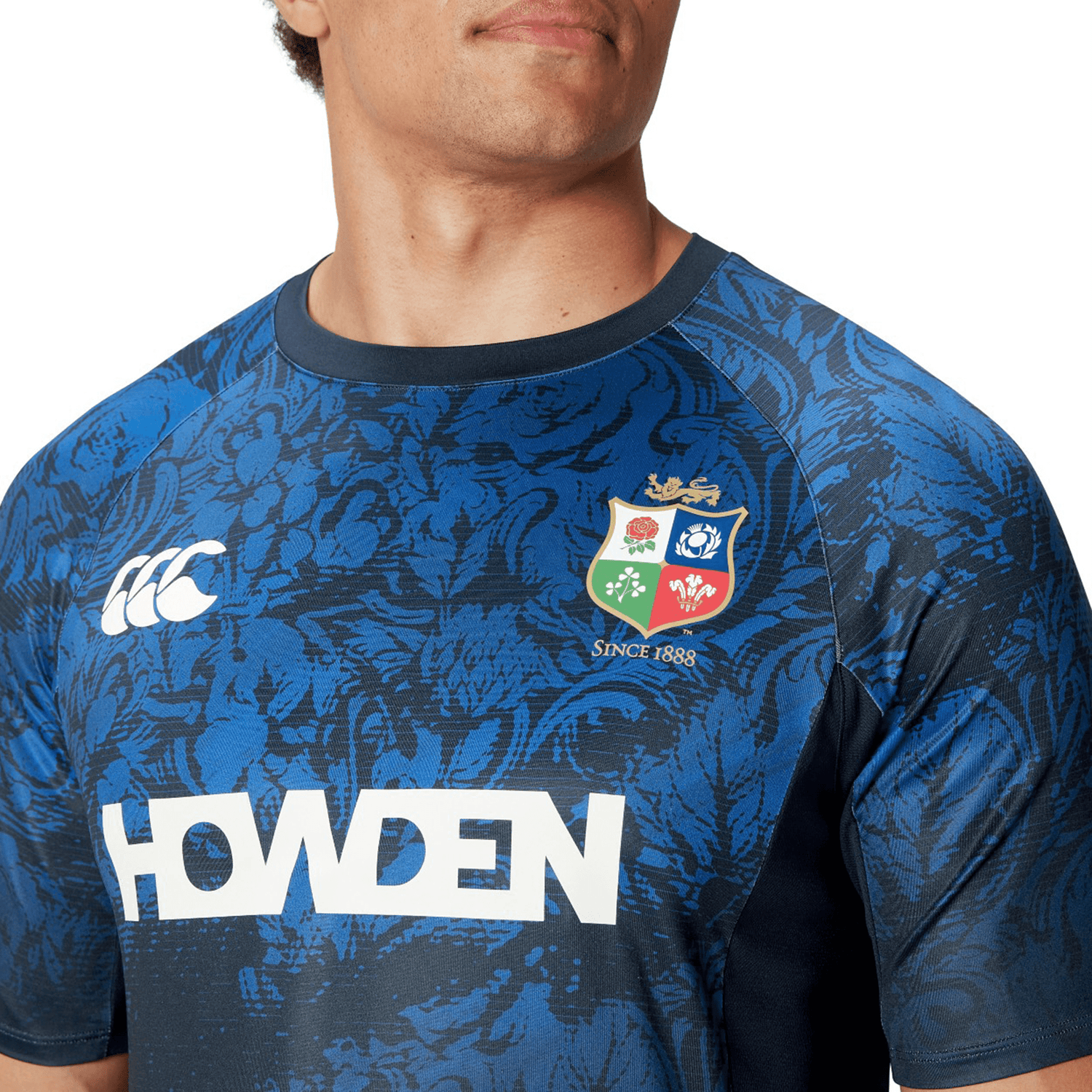A man wearing the British & Irish Lions 25 Superlight Training Tee by Canterbury captures the essence of the team with its blue design, floral patterns, team crest, and various logos.