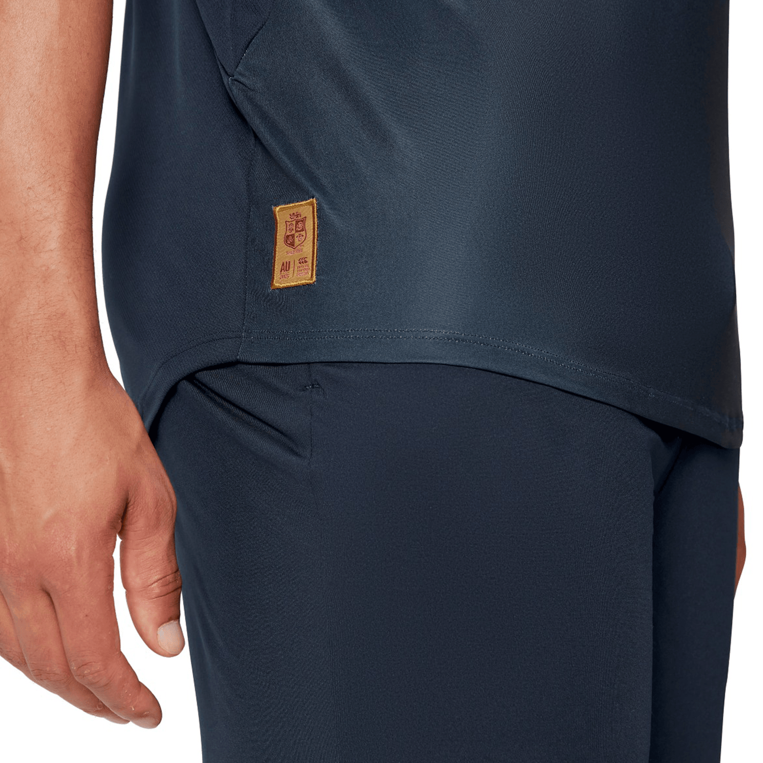 Close-up of a person wearing the British & Irish Lions 25 Superlight Training Tee by Canterbury in navy blue, showcasing part of their torso and arm. A small embroidered label with Chinese characters adds a distinctive flair, reminiscent of Canterbury's collaborations with the British & Irish Lions.