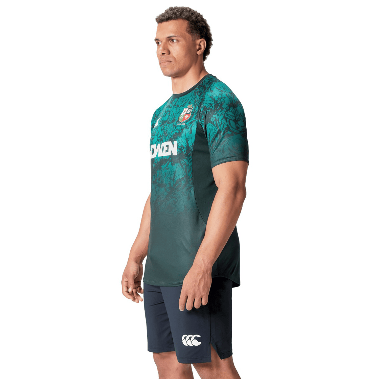 A man wearing a green British & Irish Lions 25 Superlight Training Tee by Canterbury and navy shorts stands against a plain white background, embodying the spirit of Canterbury and the iconic British & Irish Lions.