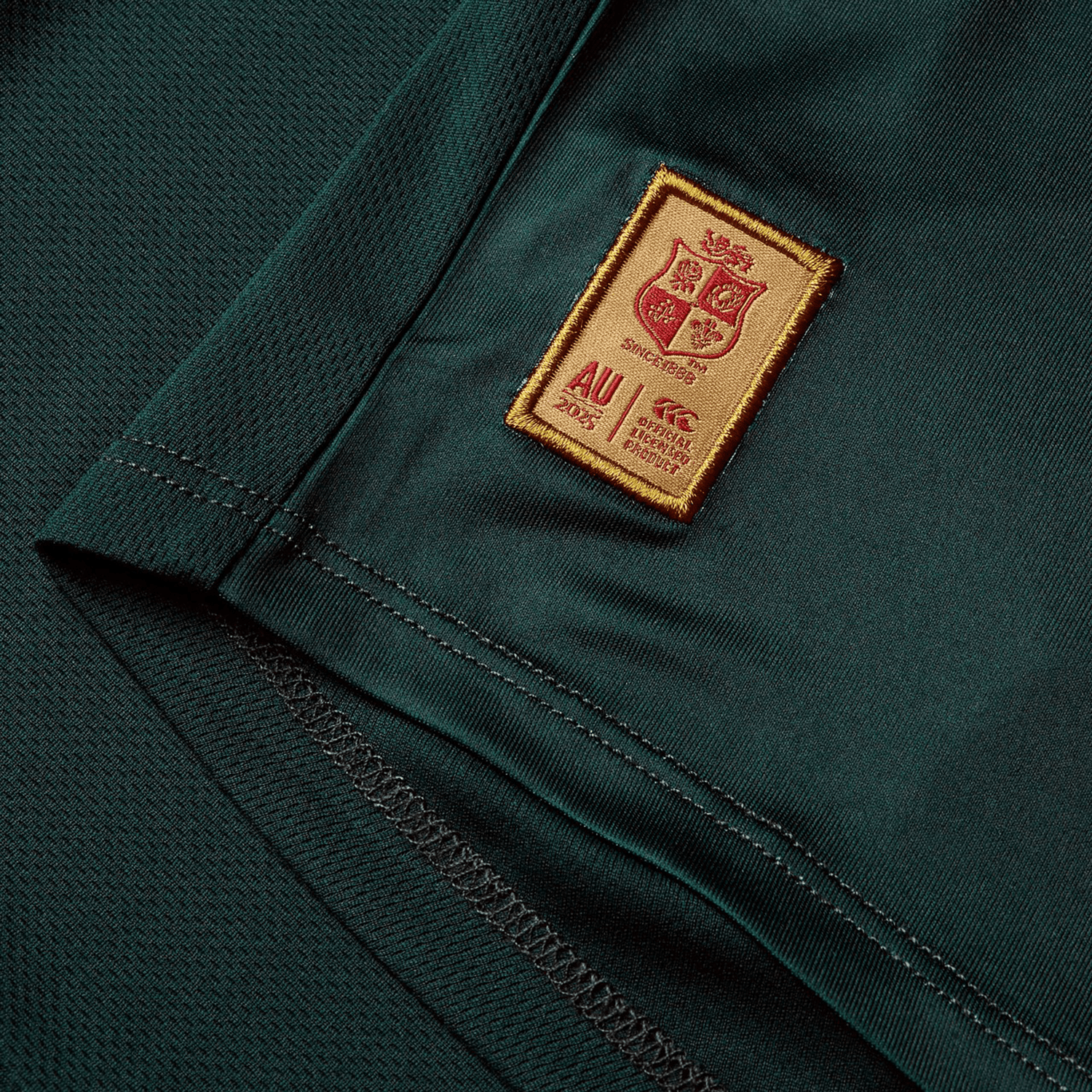 A close-up view of a deep green fabric features a sewn red and gold patch with a crest, text, and the date "AU 2023." Similar to the exceptional craftsmanship of Canterbury, this fabric showcases visible stitching and a textured pattern reminiscent of the British & Irish Lions 25 Superlight Training Tee by Canterbury.