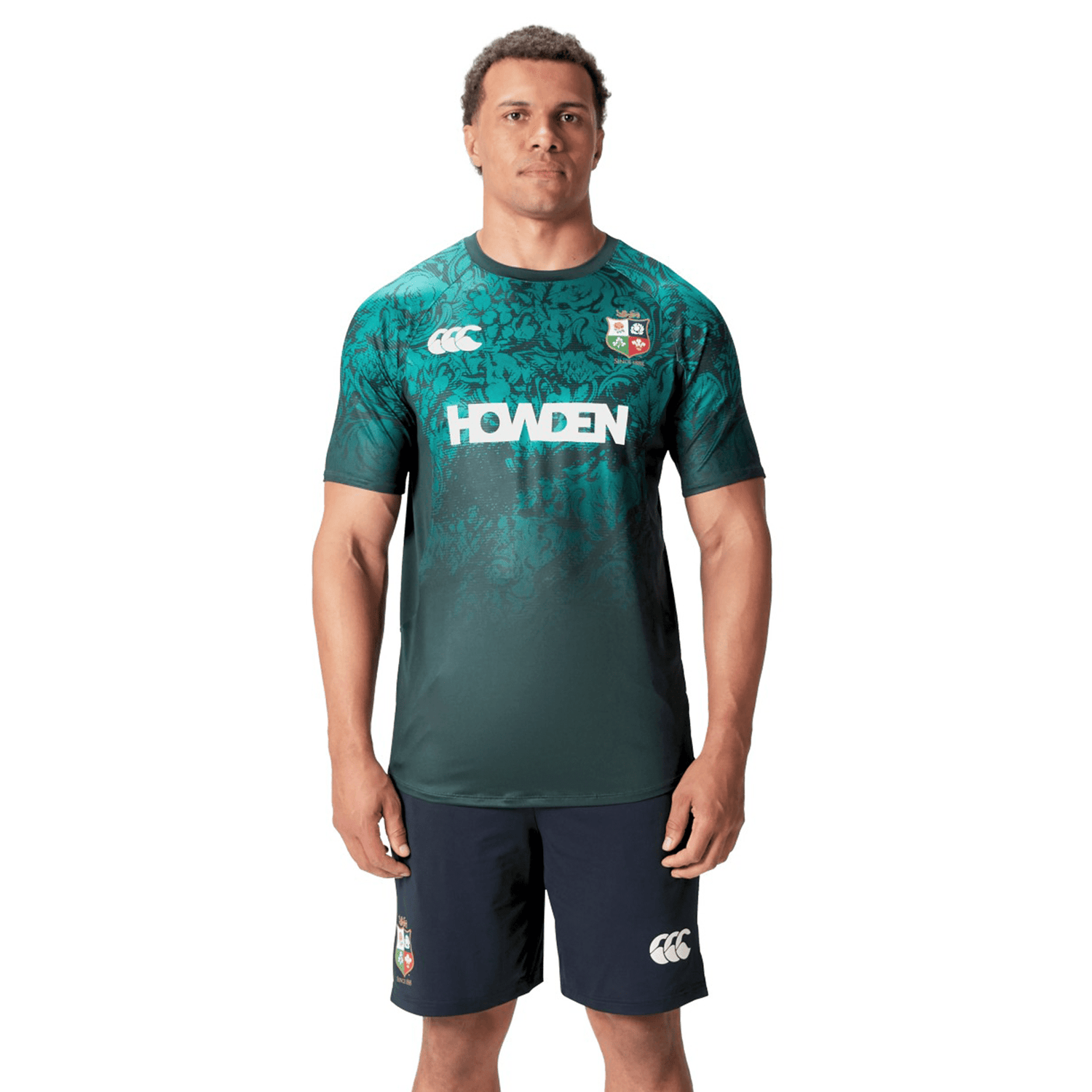 A man wearing a British & Irish Lions Superlight Training Tee by Canterbury in green and black stands facing forward in his shorts.