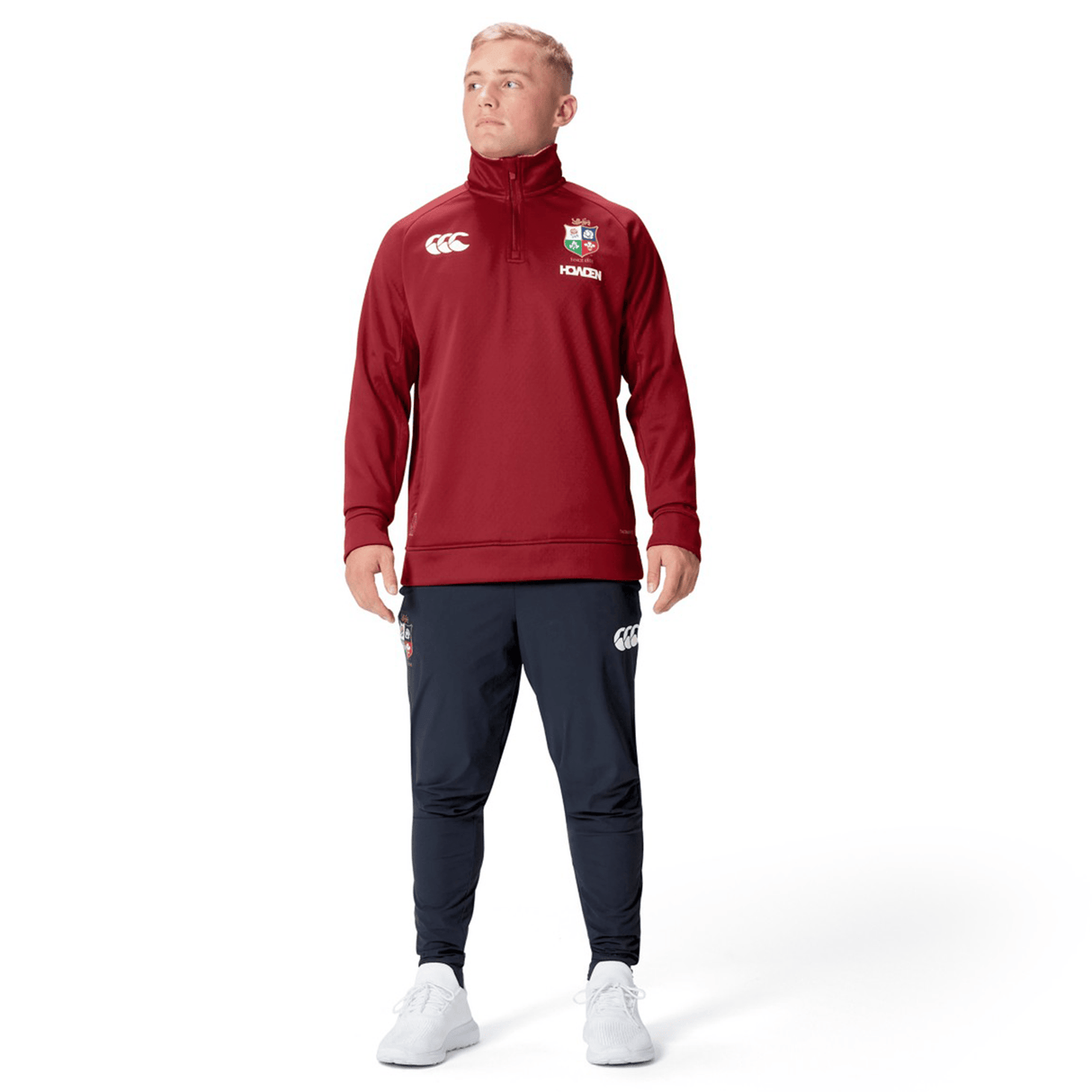 A person wearing the British & Irish Lions 2025 1/4 Zip Fleece by Canterbury in red and navy pants, standing and gazing to the side against a plain white background.