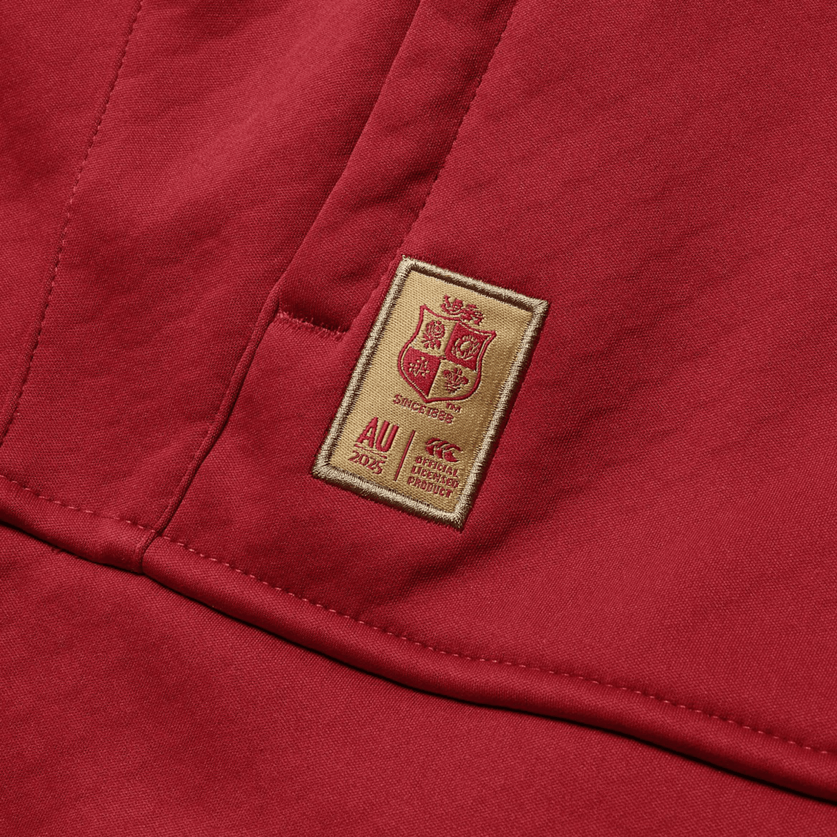 A red fabric with an embroidered patch showcasing a coat of arms, the text "AU 2023," and the phrase "Ref. Special Product." Inspired by the heritage and pride of the British & Irish Lions, this exclusive design is ideal for pairing with Canterbury's British & Irish Lions 2025 1/4 Zip Fleece.
