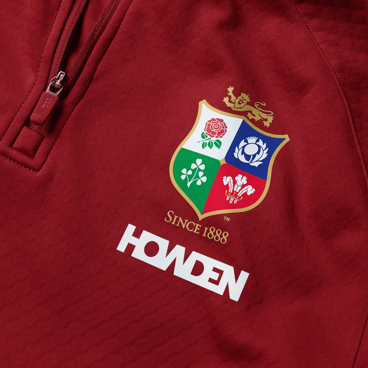 The British & Irish Lions 2025 quarter-zip fleece by Canterbury is a red top showcasing the team's crest with "Since 1888" and "Howden" gracefully printed beneath the logo.