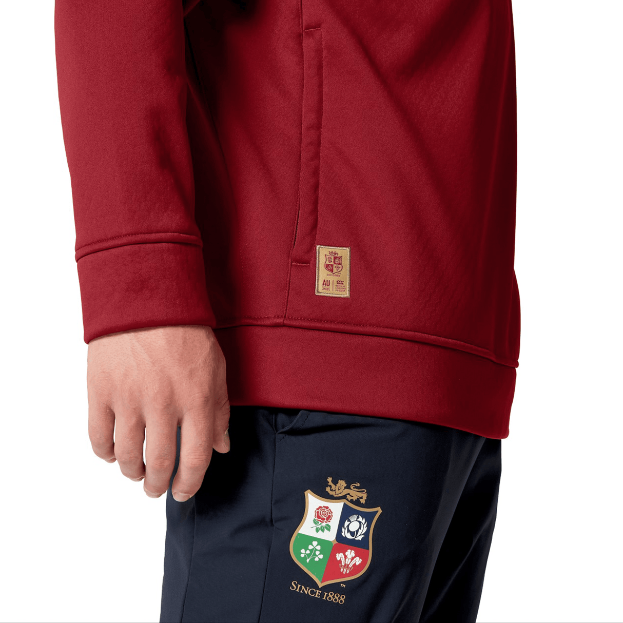A person is wearing the British & Irish Lions 2025 1/4 Zip Fleece by Canterbury, with maroon and navy colors, featuring a colorful shield emblem and "Since 1888" text, echoing the style of the team’s attire.