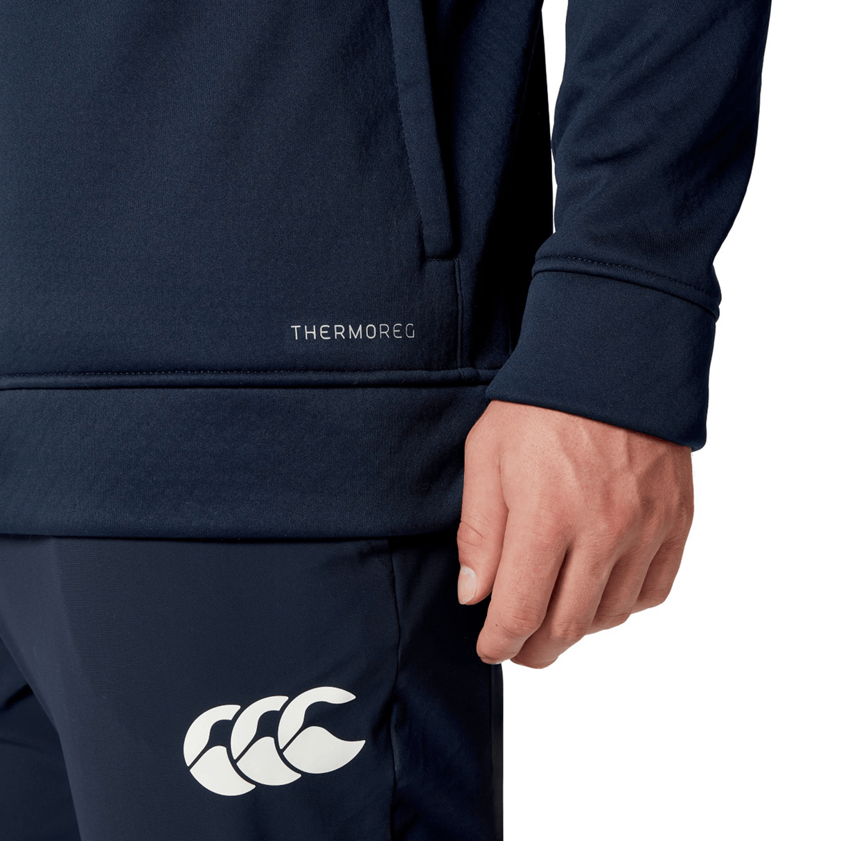 Close-up of a person wearing a navy sports outfit, showcasing the "THERMOREG" label on the top and a white logo on the pants. The British & Irish Lions 2025 1/4 Zip Fleece by Canterbury perfectly complements their look, evoking an athletic spirit reminiscent of Canterbury's celebrated apparel for the British & Irish Lions.