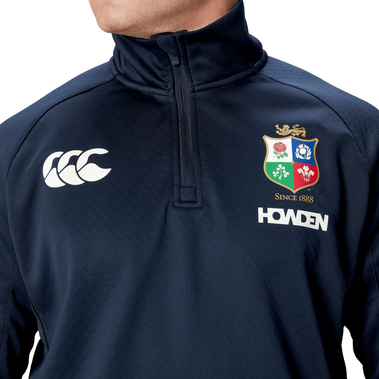 A person donning the British & Irish Lions 2025 1/4 Zip Fleece by Canterbury emanates classic charm with its stylish navy design featuring logos and embroidery, including "Howden" and "Since 1888." This fashionable piece captures the essence of Canterbury designs loved by British & Irish Lions enthusiasts, artfully merging tradition with a modern touch.