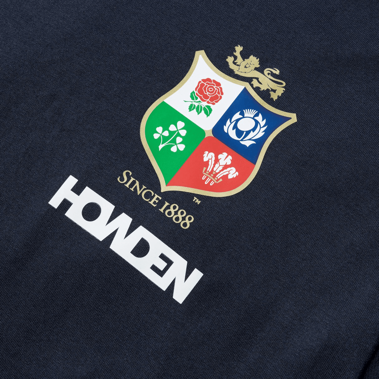 The British & Irish Lions 2025 Cotton Jersey Tee by Canterbury features a shield emblem adorned with a rose, shamrock, thistle, and dragon, accompanied by the phrases "Since 1888" and "Howden" in bold white letters. Made from organic cotton, this navy shirt delivers comfort and style for rugby enthusiasts.