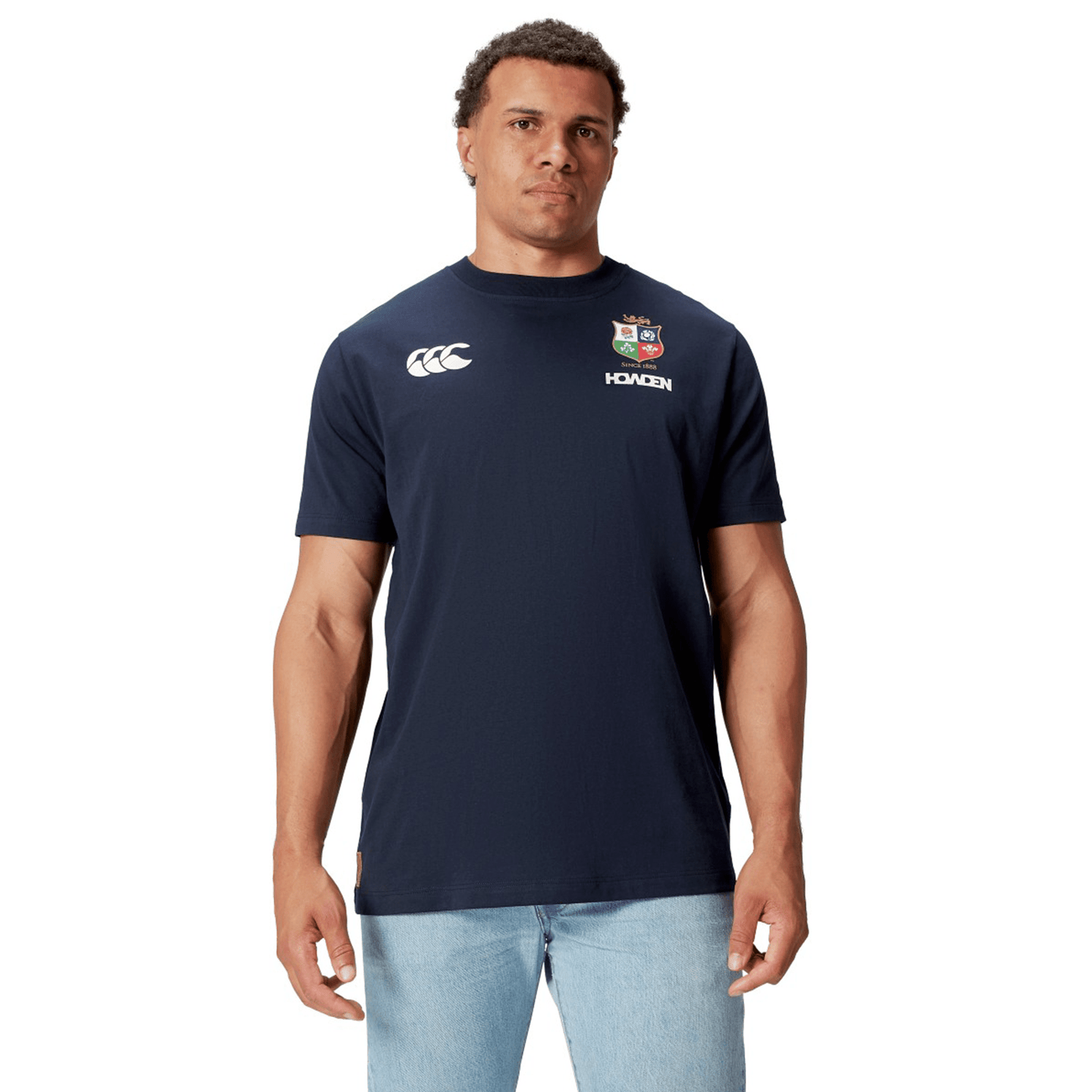 A rugby supporter proudly wears the British & Irish Lions 2025 Cotton Jersey Tee by Canterbury, paired with light blue jeans against a pristine white background.