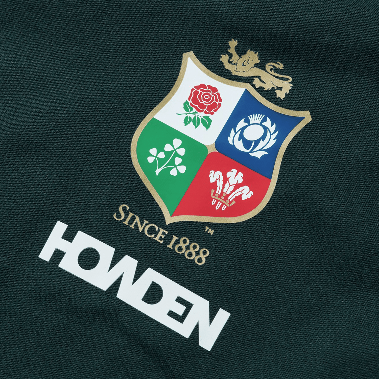 The British & Irish Lions 2025 Cotton Jersey Tee by Canterbury boasts a logo with a crest featuring a rose, thistle, clover, and a red emblem. Crafted from organic cotton fabric, it is adorned with the text "Since 1888" and "Howden," capturing the essence of rugby supporters and honoring the legacy of the British & Irish Lions.