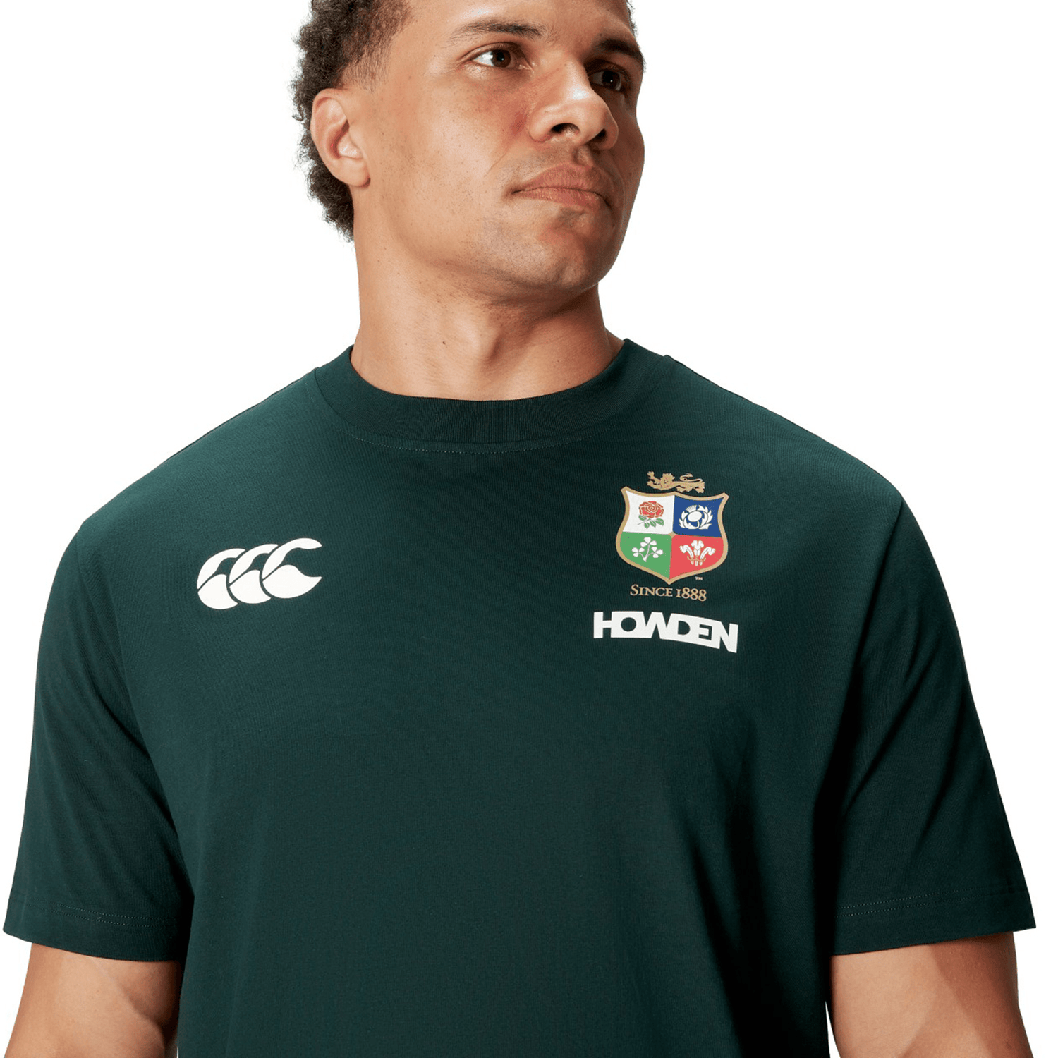 A rugby supporter wearing the British & Irish Lions 2025 Cotton Jersey Tee by Canterbury, featuring sports logos, possibly cheering for the British & Irish Lions, looks to the side.