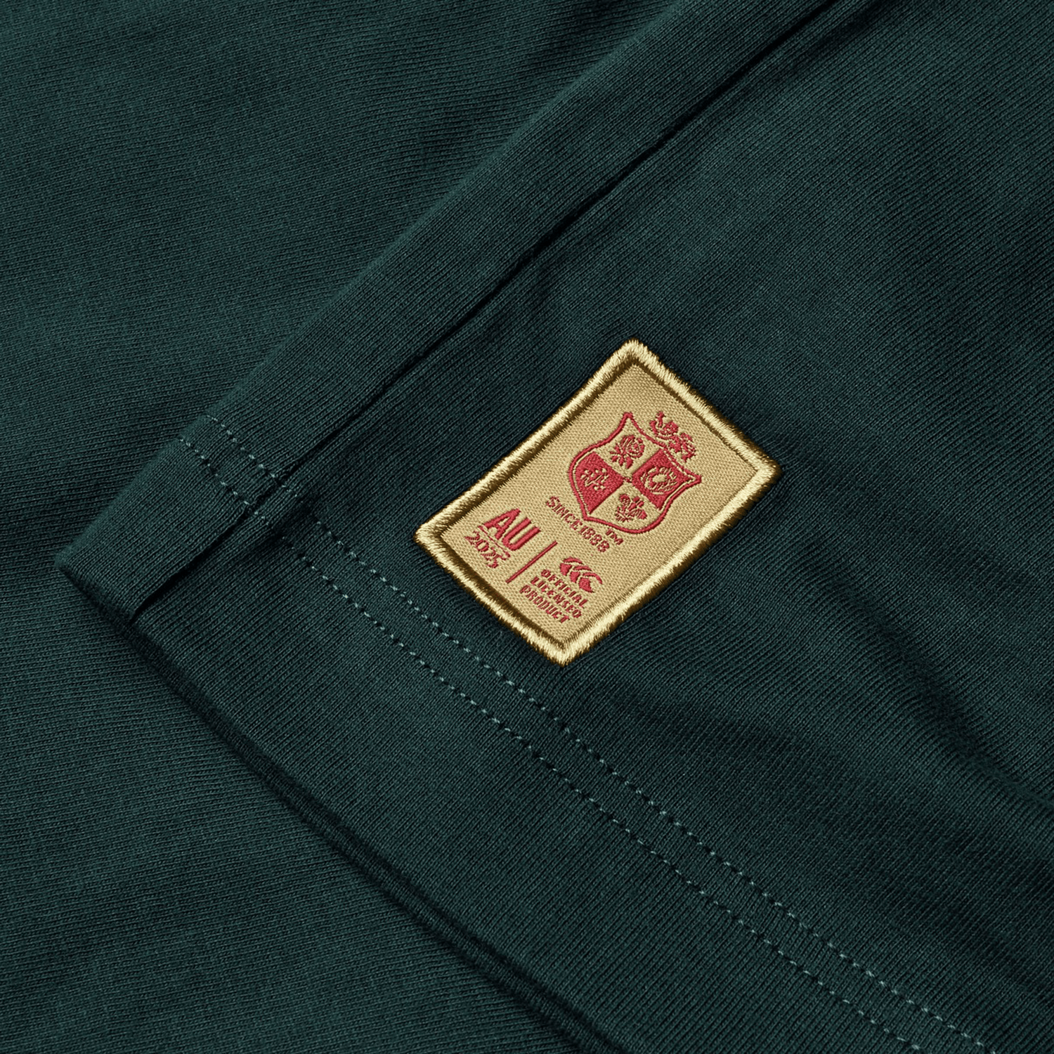 The British & Irish Lions 2025 Cotton Jersey Tee by Canterbury is crafted from organic cotton in a striking green with a distinctive brown patch, showcasing a crest and text that make it ideal for any rugby supporter.