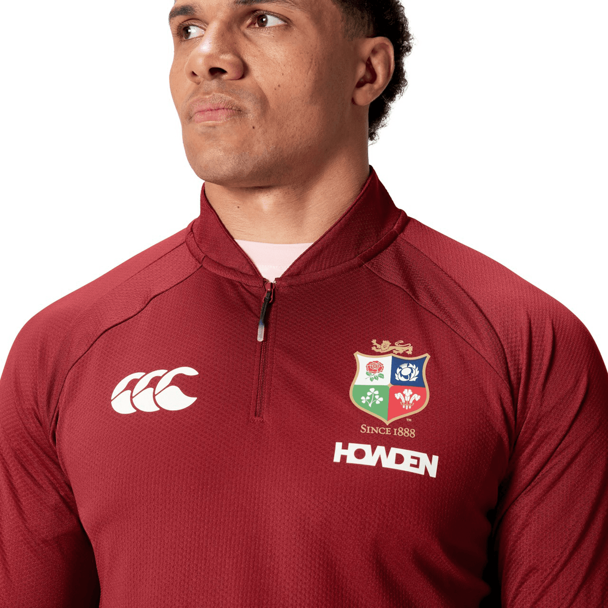 A person wearing the British & Irish Lions 25 Everest First Layer Top by Canterbury, featuring embroidered logos and a maroon color, is gazing to the side against a plain white background.