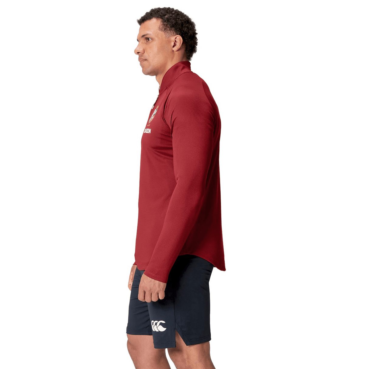 Man in a British & Irish Lions 25 Everest First Layer Top by Canterbury and dark shorts stands facing left against a white background.