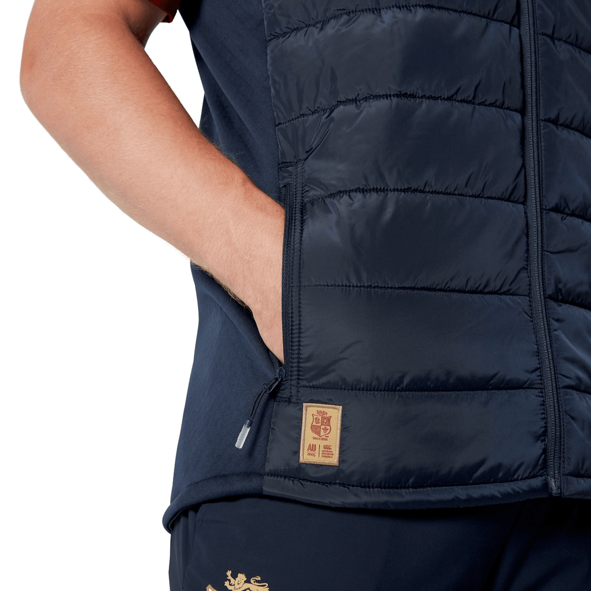 A person is wearing a navy blue British & Irish Lions 2025 Microlight Gilet by Canterbury with matching pants, hands in pockets, and showcasing the logo patch. The ensemble is crafted from Recycled Polyester, offering both style and sustainability.