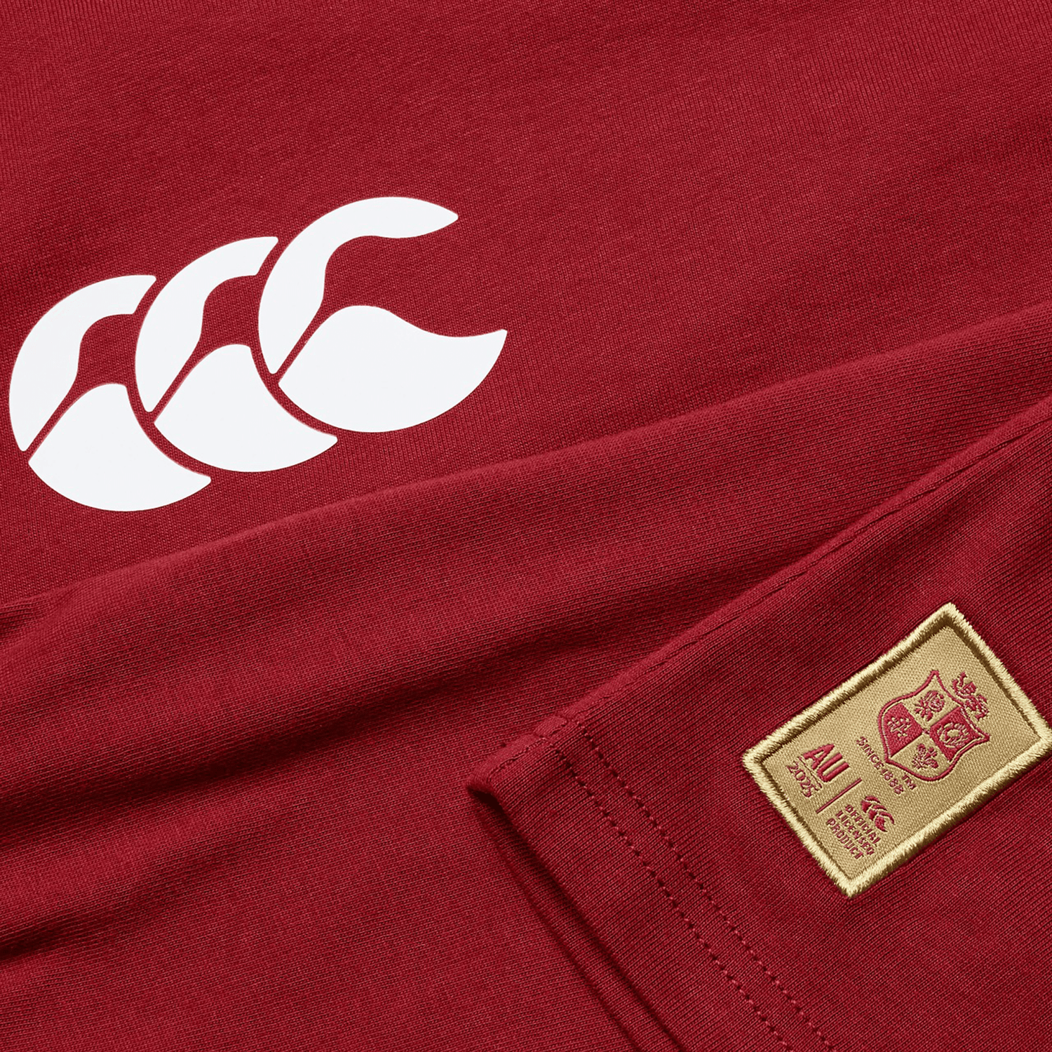 A close-up of the Women's British & Irish Lions 25 Cotton Jersey Tee by Canterbury showcases its red design made from organic cotton, highlighted by a white logo and a beige patch adorned with the British & Irish Lions crest and text.