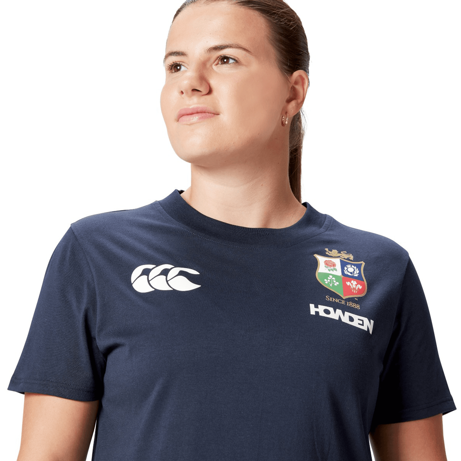 A rugby supporter in a Women's British & Irish Lions 25 Cotton Jersey Tee by Canterbury, featuring navy with sports logos, glances to the side against the white background.