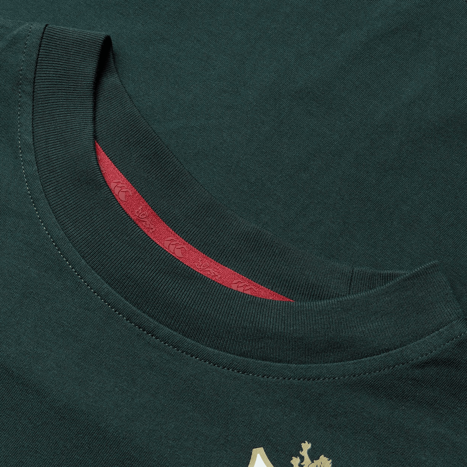 Close-up of the neckline of the Women's British & Irish Lions 25 Cotton Jersey Tee by Canterbury in dark green, made from organic cotton with a visible red inner lining. The shirt includes a small, partial gold logo at the bottom edge, making it ideal for any rugby fan who wants to express their passion subtly.