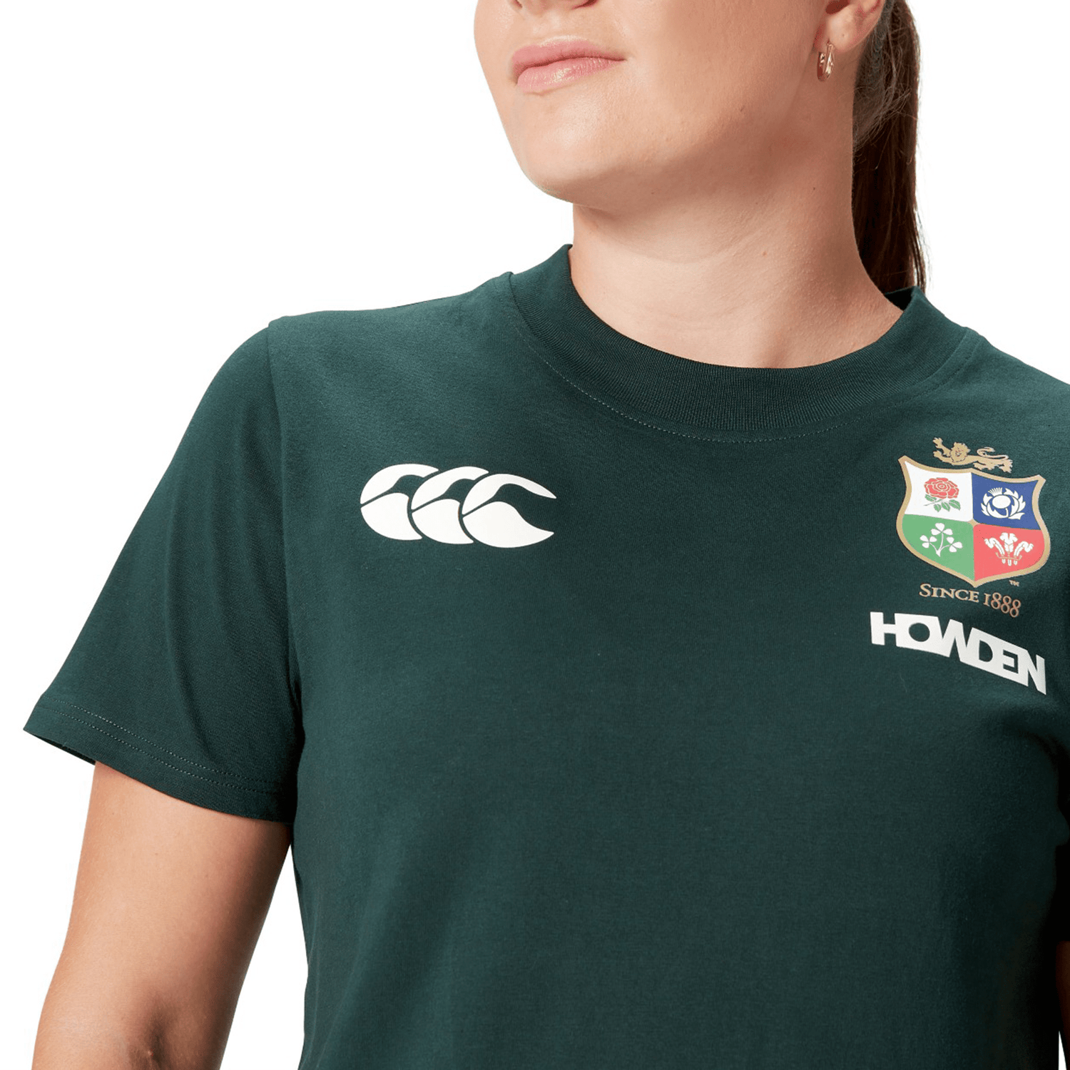 A person proudly wears a Women's British & Irish Lions 25 Cotton Jersey Tee by Canterbury in green, made from organic cotton, featuring a logo and the text "Howden" and "Since 1888.
