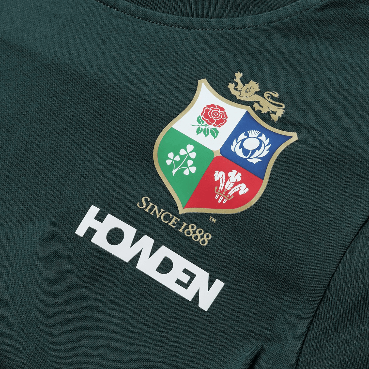 The Women's British & Irish Lions 25 Cotton Jersey Tee by Canterbury is a dark green supporter shirt made from organic cotton, featuring a multicolored crest with a lion, rose, shamrock, thistle, and dragon. Below the crest are the words "Since 1888" and "HOWDEN," making it ideal for fans of the British & Irish Lions.