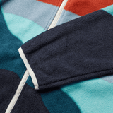 Close-up of the British & Irish Lions 2025 Outback Full-Zip Fleece Jacket by Canterbury, featuring a navy sleeve and a white zipper. The fabric displays geometric patterns in shades of red, blue, and teal, echoing the iconic styles for which Canterbury is known.
