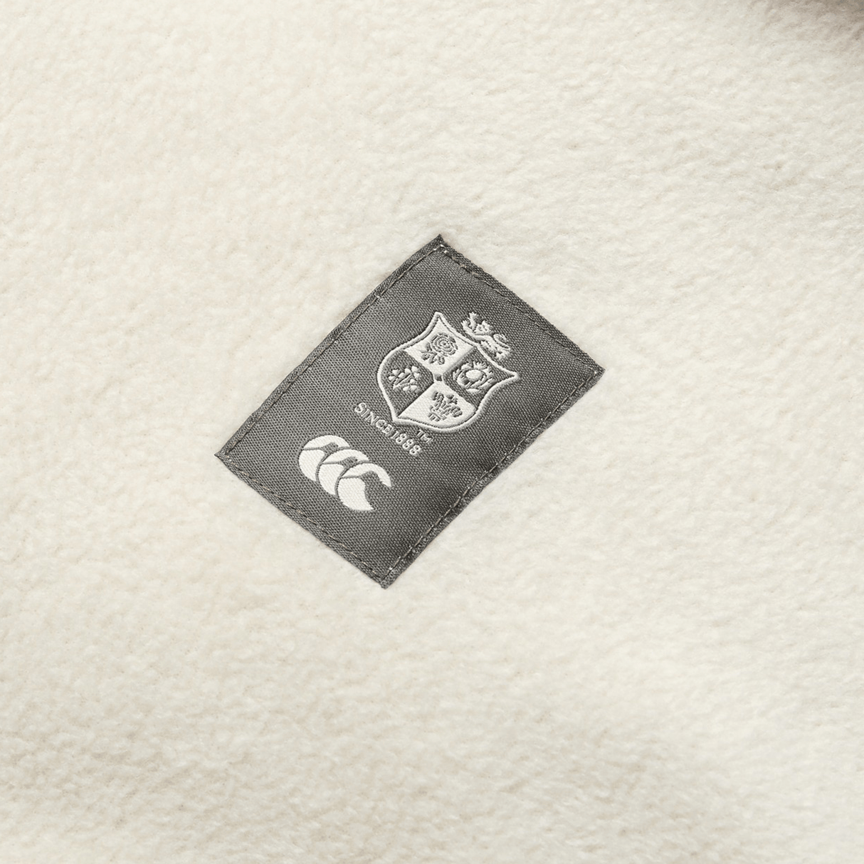 Close-up of a label on a white fabric, featuring Canterbury's iconic shield with "Since 1888" and the three overlapping crescents logo. This detail is perfect for fans of the British & Irish Lions and can be found on your favorite Canterbury British & Irish Lions 2025 Outback Full-Zip Fleece Jacket.