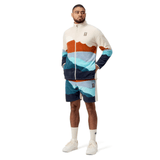 Dressed in a Canterbury British & Irish Lions 2025 Outback Full-Zip Fleece Jacket, the man strikes a pose with hands tucked into his pockets, paired with shorts featuring a bold mountain pattern. He finishes off his outfit with white socks and sneakers, capturing an adventurous spirit that echoes the essence of the British & Irish Lions.