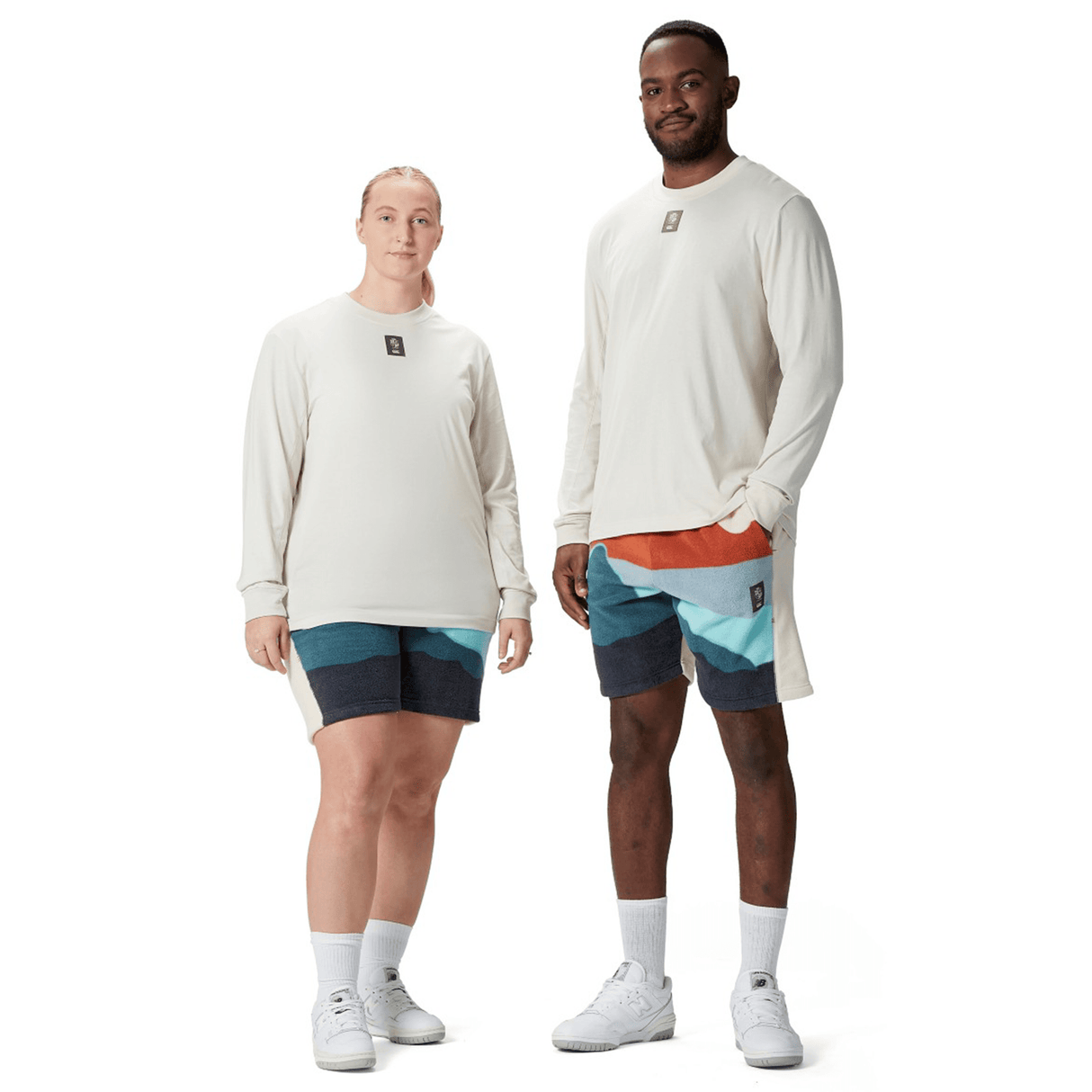 Two individuals standing together wearing Canterbury's British & Irish Lions 25 Outback Long Sleeve Tee in cream, vibrant shorts, white socks, and sneakers, evoking the striking style of the British & Irish Lions.