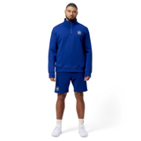 Wearing a Canterbury Sport Dept 1/4 Zip Pullover in blue and shorts, a person showcases sporty style. Complemented by white socks and shoes against a white background, the ensemble's cool tones are emphasized for a sleek look.