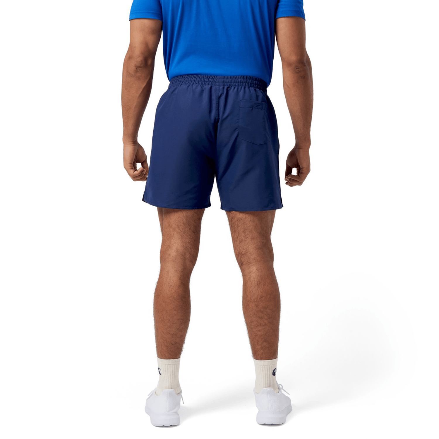 A person in a blue shirt and Canterbury Uglies 5" Tactic Short by Canterbury, featuring navy lightweight fabric and an elastic waist, stands facing away. They wear white socks and sneakers against a plain white background.