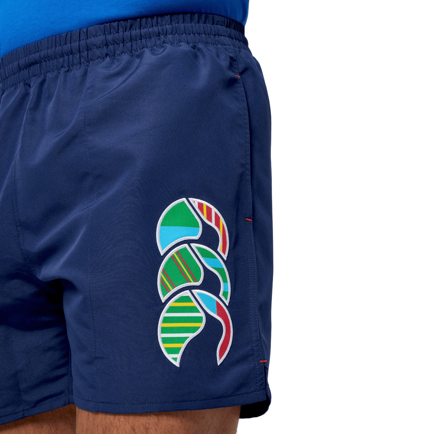 Close-up of a person wearing Canterbury's Uglies 5" Tactic Shorts in blue, featuring a colorful abstract side pattern, elastic waist for comfort, and deep pockets for convenience.