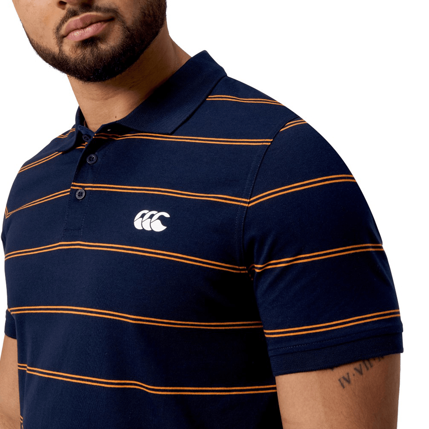 A man stands against a white background, wearing the Canterbury Fundamental Yarn-Dye Stripe Polo with bold navy and orange stripes and a chest logo.