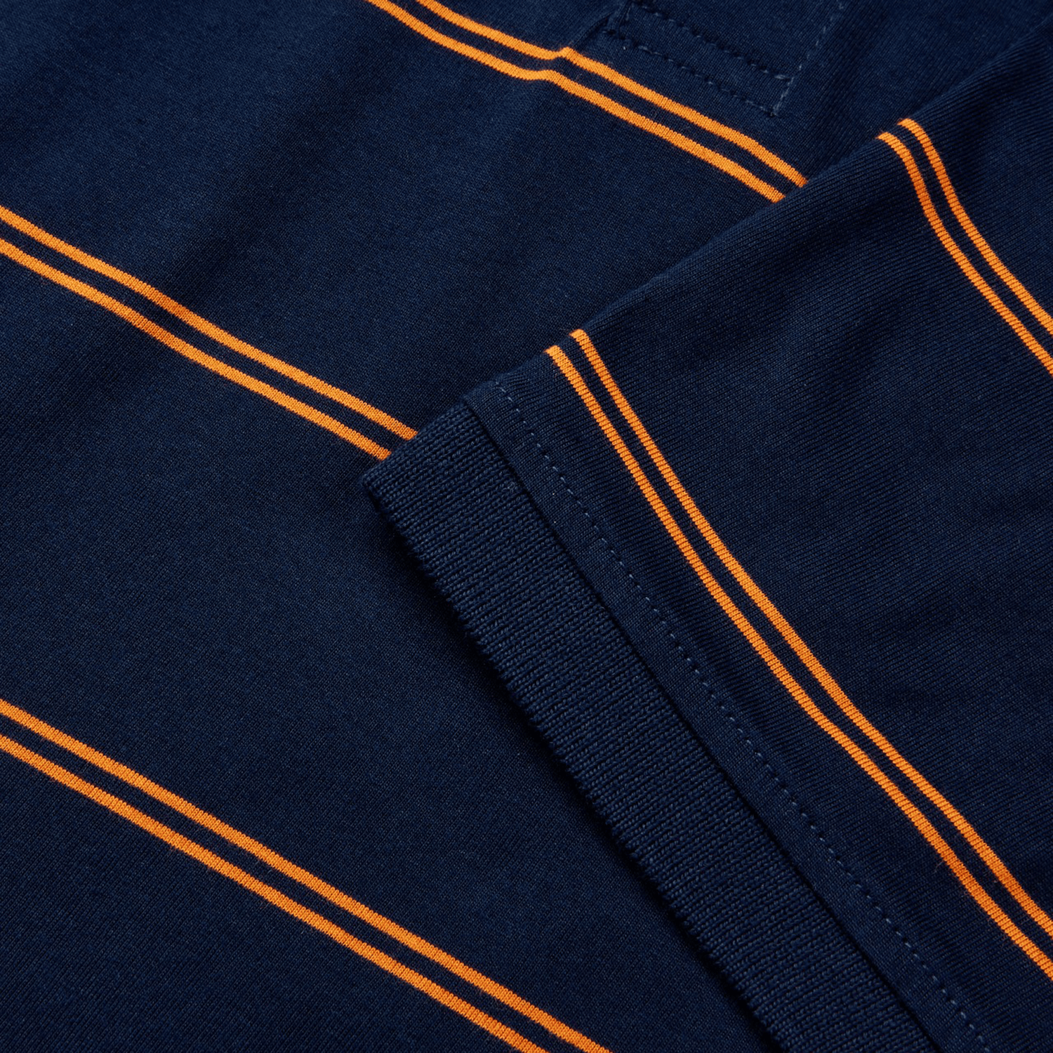 Close-up of a navy blue Canterbury Fundamental Yarn-Dye Stripe Polo, showcasing vibrant orange stripes and a neatly folded sleeve.