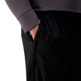 A person wearing a gray long-sleeve top and black Canterbury Tempo+ 32" Trackpant stands with their right hand in their pants pocket.
