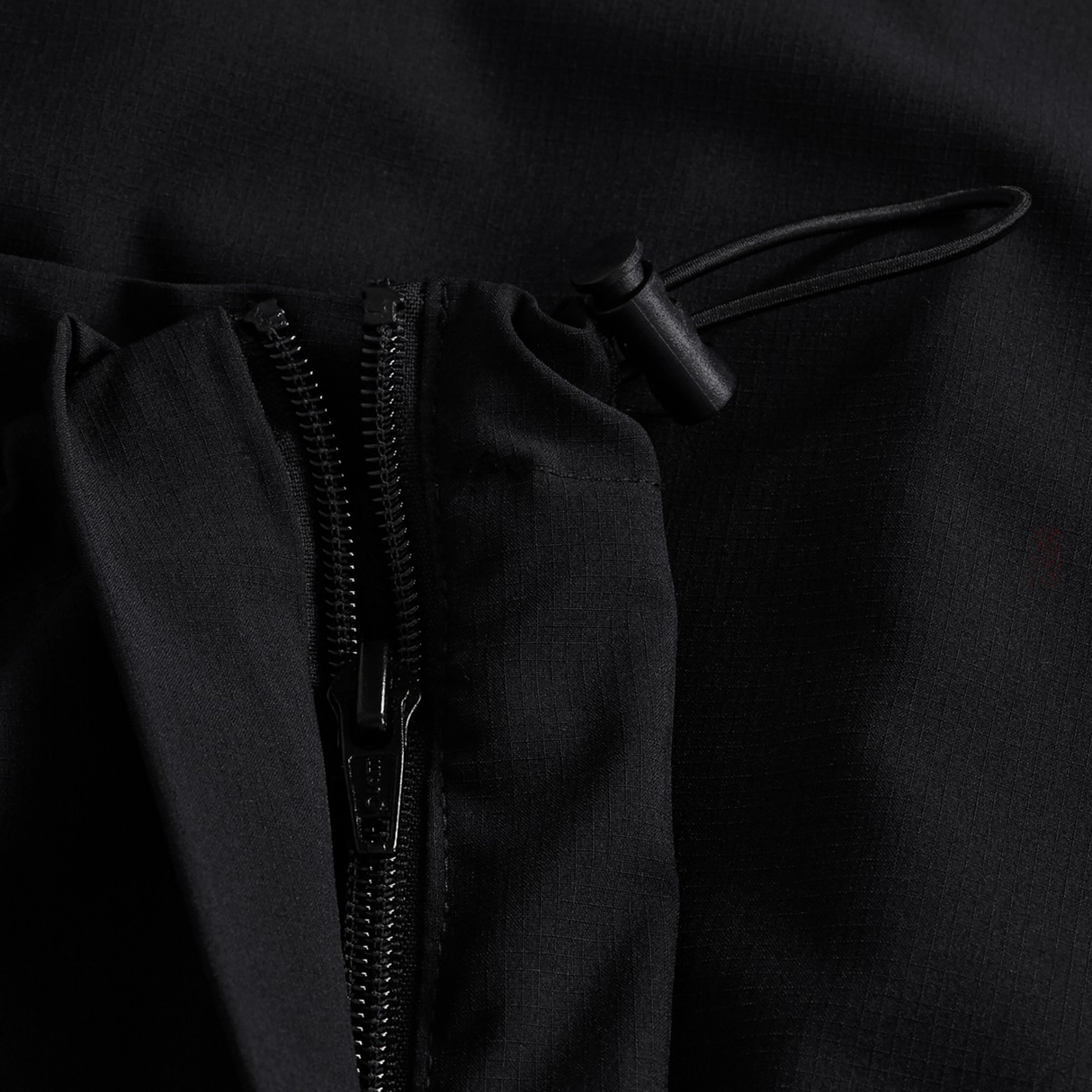 Close-up of a black fabric jacket featuring a zipper and adjustable drawstring with plastic toggle, designed to pair perfectly with the Canterbury Tempo+ 32" Trackpant for a coordinated look.