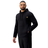 A man stands in a black Tempo+ Hoodie by Canterbury and black pants, one hand in his pocket, facing slightly to the side against a plain white background.
