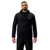 A man stands facing forward wearing a black Tempo+ Hoodie by Canterbury and black pants against a plain white background.