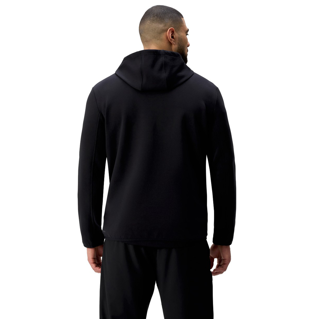 A man faces away, wearing the black Tempo+ Hoodie by Canterbury and black pants against a plain white background.