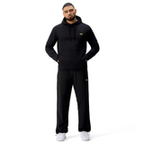 A man stands facing forward in a black Canterbury Tempo+ Hoodie and black track pants with white sneakers, set against a plain white background.